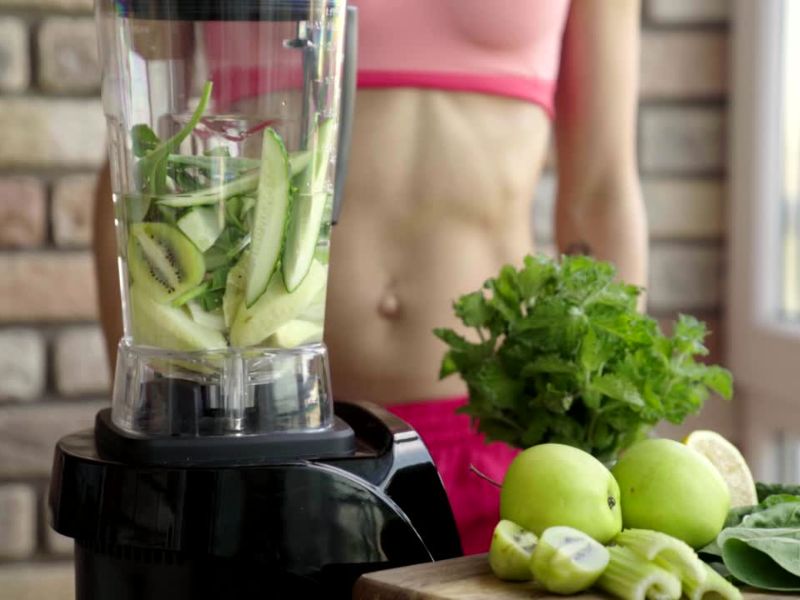 devojka pravi uz pomoć blendera zeleni smuti