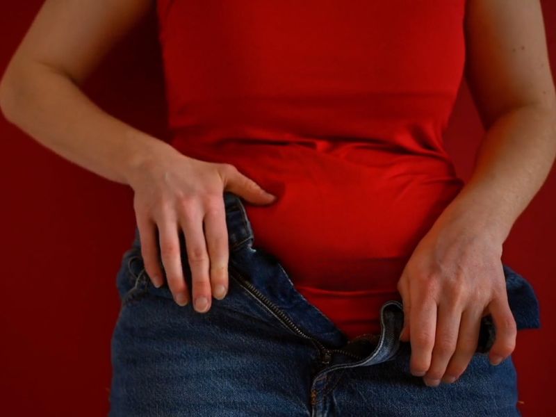 devojka koja pati od nadutosti u stomaku jedva zakopčava pantalone