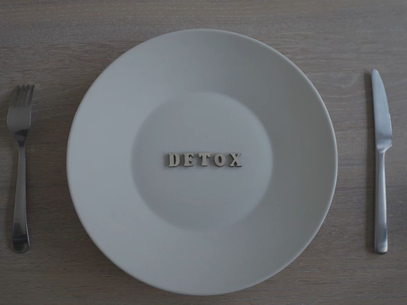 beli tanjir na kom je "detox" natpis i postavljeni nož i višljuska sa strane