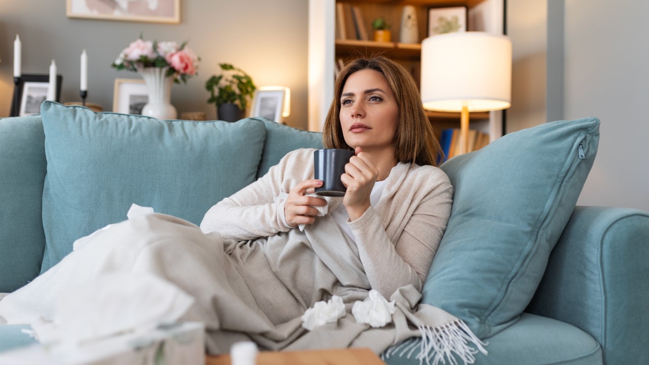Žena odmara na kauču i pije topli napitak od meda i cimeta dok ima simptome prehlade