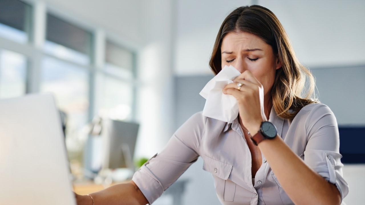 Žena u kancelariji briše nos maramicom zbog simptoma alergijske reakcije