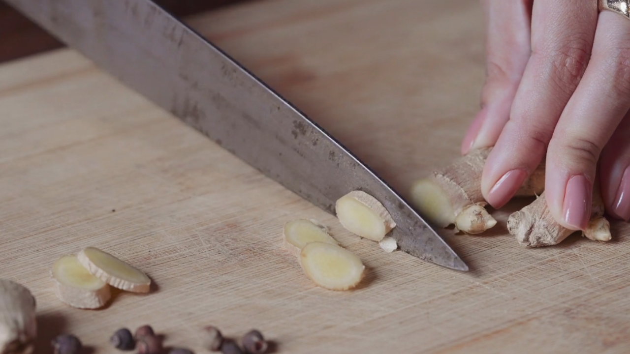 Osoba seče svež đumbir na tanke kolutove na drvenoj dasci