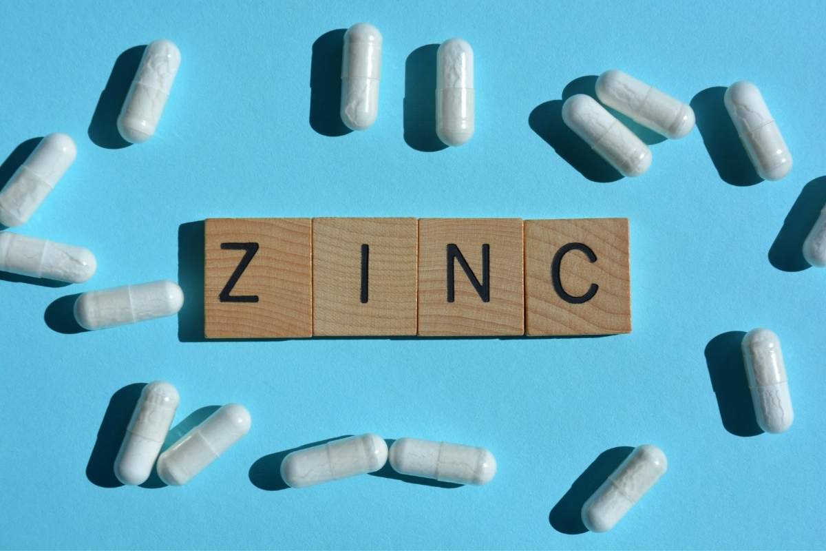 Cink za imunitet, bele kapsule suplementa raspoređene oko drvenih pločica sa natpisom ZINC na plavoj pozadini.