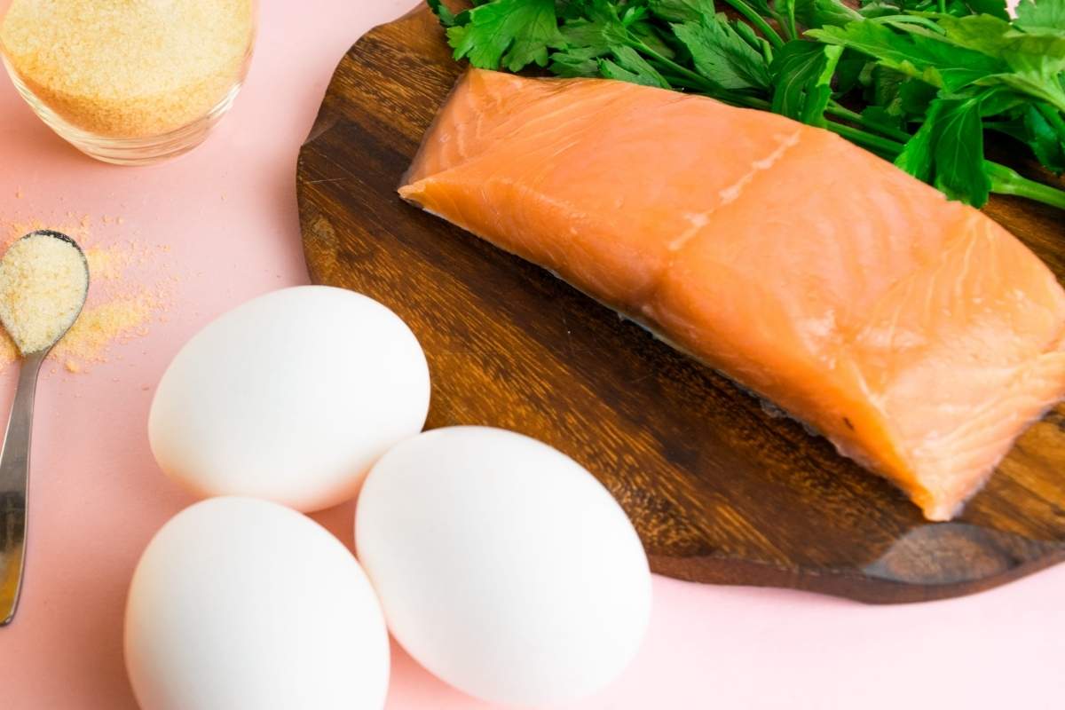 Jaja i file lososa kao prirodni izvori vitamina D, uz sveže začinsko bilje na drvenoj dasci.